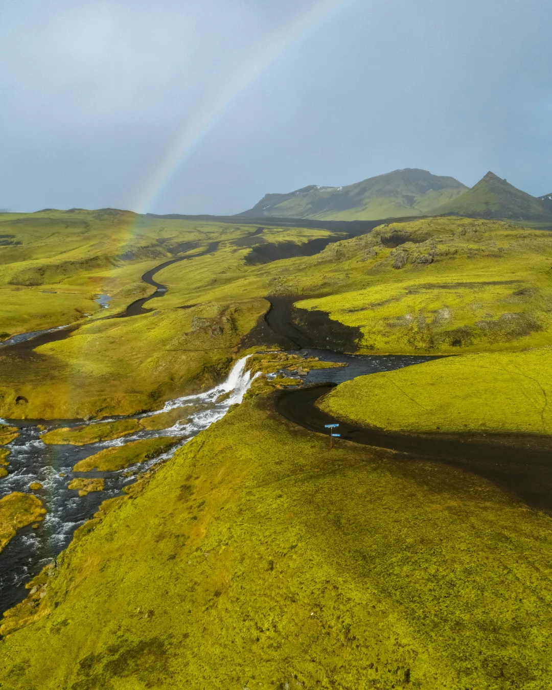 Paisaje verde con río, cascada y arcoíris en Islandia